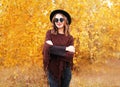 Autumn fashion portrait pretty smiling woman wearing black hat sunglasses and knitted poncho over yellow leaves Royalty Free Stock Photo