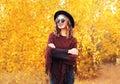 Autumn fashion portrait smiling woman wearing black hat sunglasses and knitted poncho over sunny yellow leaves Royalty Free Stock Photo