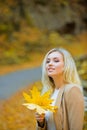 Autumn fashion trend. Young beautiful woman walking in park holding leaf. Leaves falling, fall time in nature. Royalty Free Stock Photo