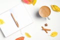 Autumn flat lay composition. Cup of coffee, opened paper notebook with pen, cinnamon sticks, fallen leaves on white wooden desk.