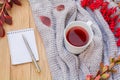 Autumn flatlay on a wooden background with a cup of tea and branches of barberry. Notepad with pen on the table. Home coziness