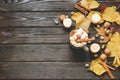 Autumn frame made of dried fall leaves, mug of cocoa with marshmellows, nuts, cinnamon, plaid, apples. Top view on brown wood back