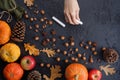 Autumn frame of pumpkins, tree leaves, hazelnuts on a black textural background. Hand with crayons for drawing. Autumn, fall,