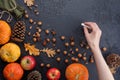 Autumn frame of pumpkins, tree leaves, hazelnuts on a black textural background. Hand with crayons for drawing. Autumn, fall,