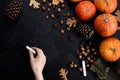 Autumn frame of pumpkins, tree leaves, hazelnuts on a black textural background. Hand with crayons for drawing. Autumn, fall,