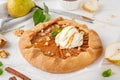 Autumn galette with pear, ice cream, walnuts, caramel sauce and cinnamon on a white wooden background