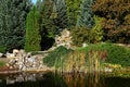 Autumn garden with artificial pond and dried out stone waterfall reflecting on water surface. Royalty Free Stock Photo