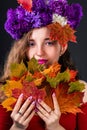 Autumn girl nymph with bright headdress of flowers and with maple leaves in her hands