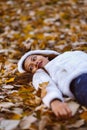 Autumn girl playing in city park. Portrait of an autumn woman lying over leaves and smiling outside in fall forest. Beautiful ener