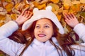 Autumn girl playing in city park. Portrait of an autumn woman lying over leaves and smiling outside in fall forest. Beautiful ener