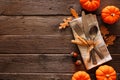 Autumn harvest or thanksgiving table scene with silverware, napkin, leaves and pumpkin border against a rustic wood background