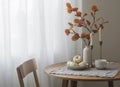 Autumn home interior in the living room - around wooden table, a chair, a bouquet of autumn leaves in a vase, decorative pumpkins Royalty Free Stock Photo