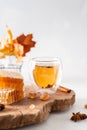 Autumn hot tea with ginger and cinnamon in a glass tea cup, honey combs and autumn leaves on a wooden tray on white background.