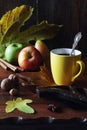 Autumn image: Yellow cup of coffee, nuts, autumn leaves and apples