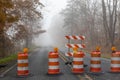 Autumn landscape with closed and barricaded road fading into dense fog, transportation theme with traffic barrels Royalty Free Stock Photo