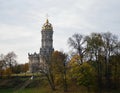 An autumn landscape in gold and green, bare trees, with an old baroque church, and a newly married couple