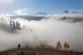 Autumn landscape of high mountains, orange coloured trees, fog. Sun rays enlighten the lawn with dry grass. Blue sky. Royalty Free Stock Photo