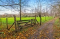 Autumn landscape with hiking path along a green meadow with wooden rural gate in Belgium. Royalty Free Stock Photo