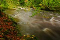 Autumn landscape with orange and yellow leaves in the water, big rock in the background, Kamenice river, in czech national park Royalty Free Stock Photo