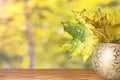 Autumn leaves in a gold vase on a wooden table