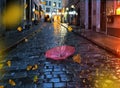 Autumn leaves pink umbrella on wet pavement at rainy medieval evening street light plurred reflektion rain fall