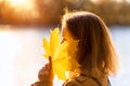 Autumn maple leaf in hand of pretty woman, portrait outside in autumn season. Beautiful fall nature, scene by river in autumn park