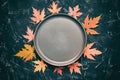 Autumn modern minimal composition. Empty plate and frame made of red dry maple leaves on a black stone background, toned. Top view