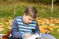 Autumn mood. The boy is thoughtfully drawing something in his notebook.Autumn portrait of a child in yellow foliage. Sight. Cute Royalty Free Stock Photo