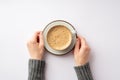 Autumn mood concept. First person top view photo of female hands in grey sweater holding saucer with cup of frothy coffee on Royalty Free Stock Photo