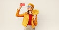 Autumn mood! woman taking selfie picture by phone blowing red lips sending sweet air kiss holding yellow maple leaves Royalty Free Stock Photo