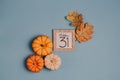 Autumn October flat lay. Orange mini pumpkins and calendar date in wooden frame. Halloween day. Blue background. Oak leaves. Fall