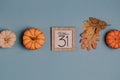 Autumn October flat lay. Orange mini pumpkins and calendar date in wooden frame. Halloween day. Blue background. Oak leaves. Fall