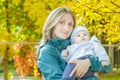 Autumn outdoor happy mother portrait holding her baby at yellow autumn shrubbery leaves background Royalty Free Stock Photo