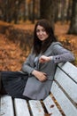 Autumn outdoor portrait of young woman in autumn park, sitting on a white bench and enjoying the fall landscape,wearing