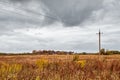 Autumn panoramic landscape with wooden houses, field and dramatic clouds. Wires.