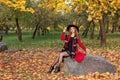 In an autumn park a girl sits on a rock in a red coat with a black hat and scarf Royalty Free Stock Photo