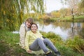 In the autumn park, a mother and daughter sit on the shore of the lake under the willows