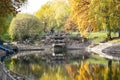 Autumn Park, trees reflected in the pond white rusty fence, withered leaves, stone waterfall Royalty Free Stock Photo