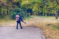 In the autumn park worker removes the road from the fallen leaves with help