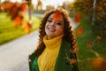 In the autumn park with yellow and crimson leaves there is a smiling beauty in a yellow sweater and green coat