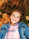 Autumn portrait of adorable smiling little girl child preteen lying in leaves in the park