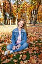 Autumn portrait of adorable smiling little girl child preteen sitting in leaves in the park