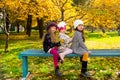 Autumn portrait of beautiful children on the bench. Happy little girls with leaves in the park in fall.