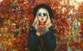 Autumn portrait of beautiful young woman blowing her lips sends sweet air kiss wearing black round hat, sunglasses and coat jacket Royalty Free Stock Photo