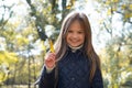 Autumn portrait of cute little blond girl in city park. Beautiful laughing child holding a yellow leaf, having fun Royalty Free Stock Photo