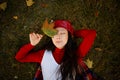 Autumn portrait. Happy asian girl in a leather hat and red sweater is lying on the ground in the park with yellow leaves Royalty Free Stock Photo