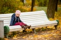 Autumn portrait of sad lonely child girl sitting on bench in park in warm blue coat and hat,enjoying outdoor walk in Royalty Free Stock Photo