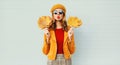 Autumn portrait woman holding yellow maple leaves blowing red lips sending sweet air kiss in french beret posing over gray wall Royalty Free Stock Photo