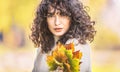 Autumn portrait of young woman with curly hair and bouquet of maple leaves