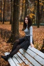 Autumn portrait of young woman in autumn park, sitting on the back of a white bench and enjoying the fall landscape